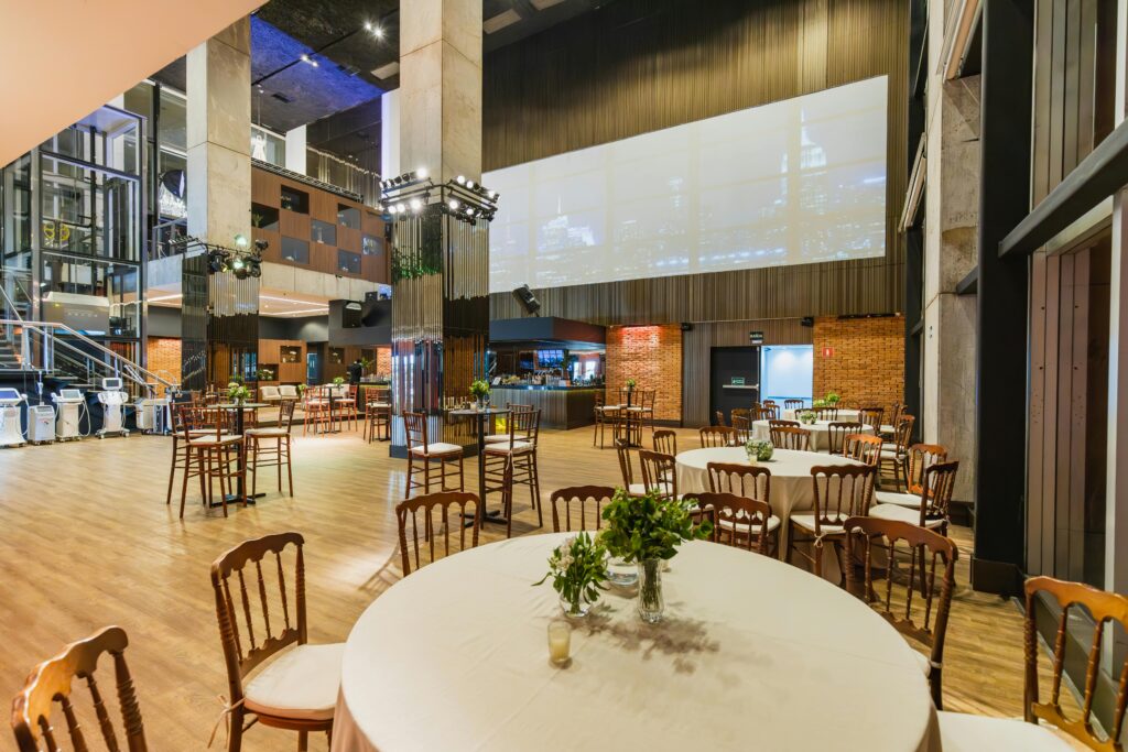 Spacious and elegantly decorated event hall with round tables and wooden chairs ready for a celebration.