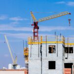 Home Tower cranes at a construction site working on a high-rise building under a clear blue sky.